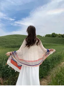 Outdoor detail shot of a woman wearing a colorful striped shawl in a green natural landscape.