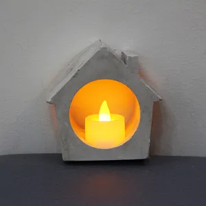 Close up of concrete house tealight candle holder with warm LED light for home decor detail.