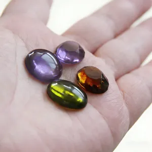 Handgehaltene Präsentation farbiger ovaler Harz-Edelstein-Cabochons, glänzend und glatt.
