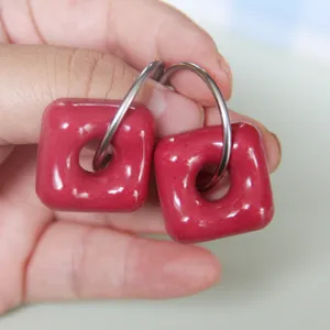 Close-up detail of red square donut hoop pendant earrings showing glossy resin texture.