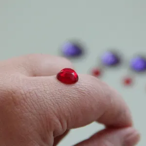 Detailansicht eines kleinen roten facettierten Edelstein-Cabochons auf einem Finger.