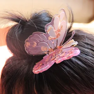 Close-up detail shot of a translucent pink butterfly hair clip with shimmering gold foil.