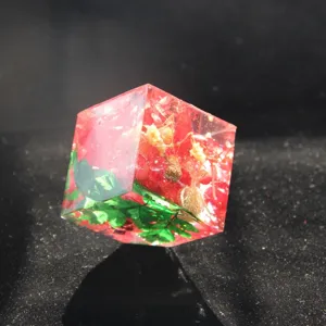 Dettaglio ornamento cubo in resina epossidica con fiori rossi e foglie verdi