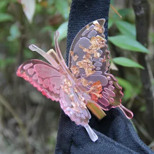Detailed close-up of a pink butterfly hair clip with gold foil resin accent outdoors.