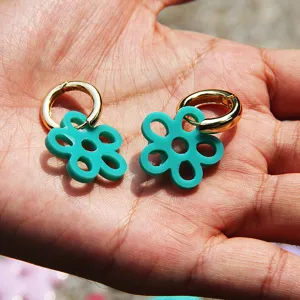 Nahaufnahme von stylischen türkisen Blumen-Creolen auf der Handfläche, minimalistisch.