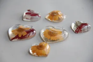 Primo piano di ciondoli in resina a forma di cuore con veri fiori secchi all'interno per decori.
