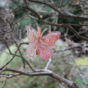 Close-up detail shot of a pink resin butterfly hair clip with gold flakes, clipped on branches.