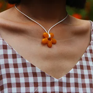 Close-up view of handmade orange resin flower pendant necklace on white cord.