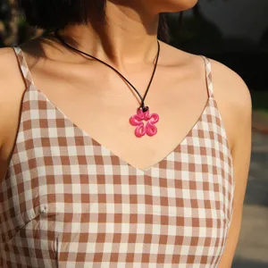 Close-up detail shot of the pink resin flower pendant necklace with black cord for women.