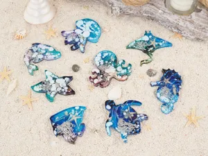Details of marine animal resin charms with jellyfish, turtle, and starfish on sandy background.