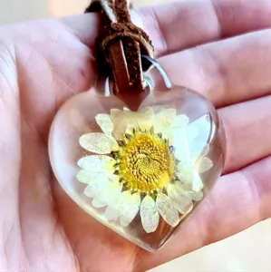 Ciondolo a cuore in resina trasparente con margherita essiccata su cordoncino marrone.