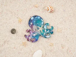 Detailed close-up of a handmade octopus resin piece with ocean elements on sandy beach.