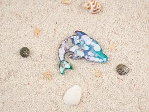 Close-up detail of a beautiful resin dolphin craft piece on a sandy beach with seashells.
