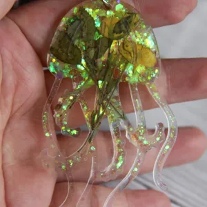 Handgefertigter transparenter Epoxidharz-Quallen-Anhänger mit getrockneten Blumen und Glitzer.