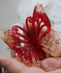 Handgemaakte rood en doorzichtige hars vlinderornament met glinsterende goudvlokken.