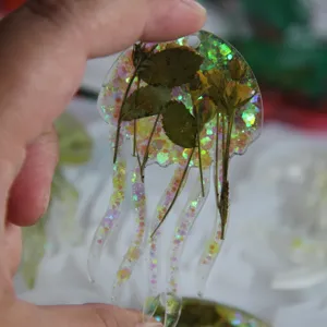 Handgefertigter Quallen-Harzanhänger mit zarten Trockenblumen und glitzernden Details.