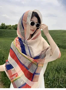 Outdoor detail view of a colorful geometric striped fashion shawl scarf worn by a model in nature.