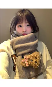 Close-up detail of cozy knitted winter scarf featuring cute plush teddy bear and plaid bow.