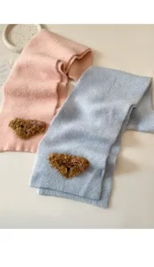 Close-up of fluffy knitted scarf featuring cute bear applique, soft winter neck warmer detail.