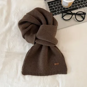 Detailed view of a cozy brown knit scarf featuring a soft texture and a stylish small leather label.