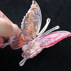 Close-up detail of a pink translucent 3D butterfly hair clip with shimmering gold foil flakes.