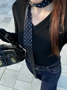 Gros plan détaillé d'un foulard étroit noir à pois chic assorti avec un haut noir.