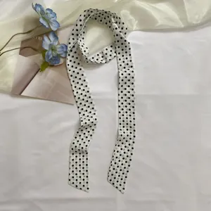 Détail d'un foulard en soie long et étroit à pois noirs et blancs, accessorio élégant.