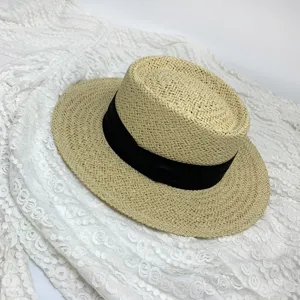 Close-up of summer woven straw boater hat with black ribbon, elegant wide brim sun hat detail.