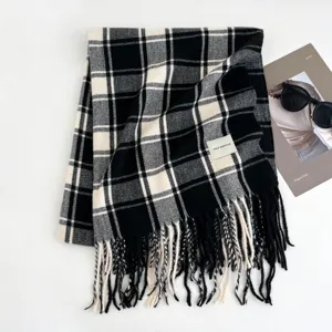 Detailed view of a classic black and white plaid scarf with cozy tassels and a minimalist brand label.