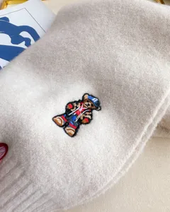 Close-up detail of beige knit wool scarf featuring cute embroidered bear pattern, winter warm.