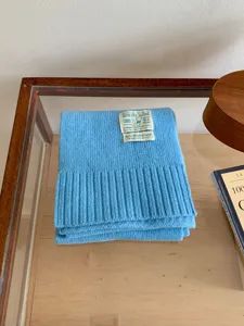 Vue détaillée d'une douce écharpe en tricot bleu lac avec ourlet côtelé et étiquette.
