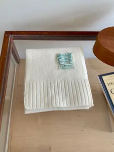 Gros plan d'une écharpe en tricot blanc pliée proprement sur table en bois avec accessoires.