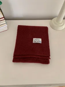 Detail shot of a dark red knitted winter scarf, neatly folded with a small brand label.