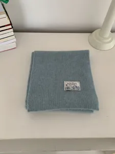Close-up detail of a cozy blue knit scarf folded neatly on a clean white tabletop.