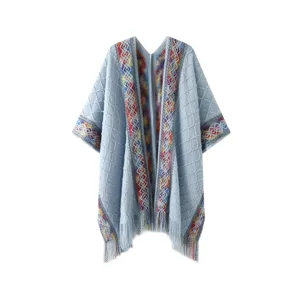 Detailed view of women light blue knit poncho, featuring colorful woven geometric patterns and fringe hem.