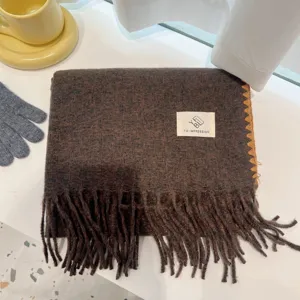 Detailed view of the dark brown winter warm fringed scarf with textured fabric and brand label.