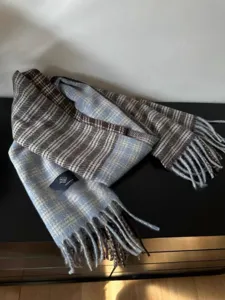 Vue détaillée de l'écharpe d'hiver à carreaux bleus et marrons, texture douce et franges.