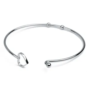 Silver metal open cuff bracelet detail view with hollow heart charm and small beads.