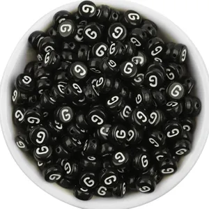 Detail view of black acrylic flat round letter beads with white letter G in white bowl for DIY.