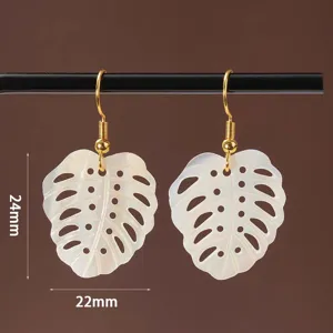 Detailopname van witte schelp monstera blad oorbellen met goudkleurige haken, fijn ajour.