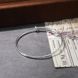 Close-up detail of a minimalist silver adjustable metal coil bangle bracelet on dark surface.