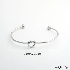Pulsera de brazalete abierto de acero inoxidable con diseño de nudo de corazón minimalista.