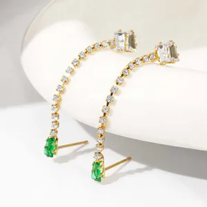 Detailopname van lange vergulde zirkonia oorbellen met groene steenhangers.