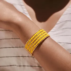 Detailopname van een meerstrengs gele kralenarmband met gouden metalen afstandshouders.