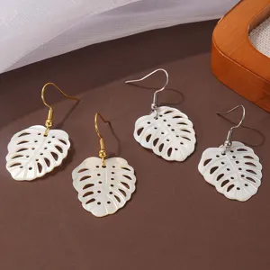 Close-up detail van witte schelp monstera blad oorbellen met gouden haken.