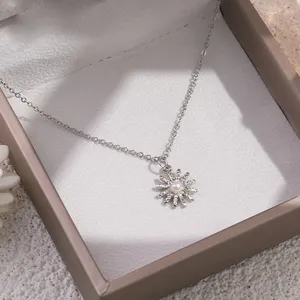 Gedetailleerde close-up van een delicate zilveren bloemenhanger ketting met kleine parel.