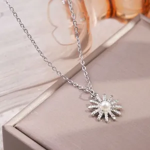 Detailopname van een zilverkleurige ketting met een parel zonnebloemhanger en glinsterende steentjes.