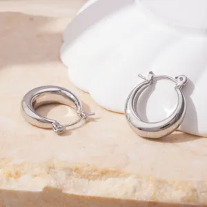 Close-up of minimalist chunky silver metal hoop earrings on textured stone background.