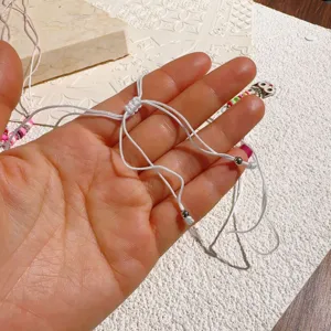 Detail van de verstelbare witte gevlochten koordketting met schuifknoop en metalen kraaltjes.