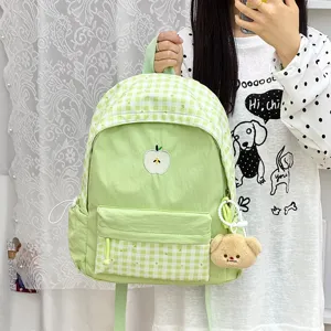 Sac à dos d'écolier à carreaux vert clair frais avec broderie de pomme et charmant pendentif d'ours.